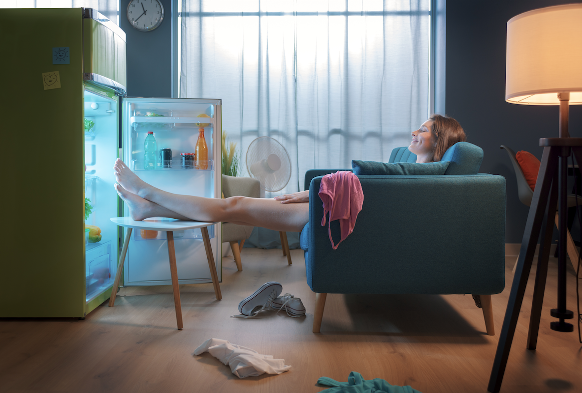 picture of a person sitting on a couch with her feet in the refrigerator to keep cool during a hot summer. 