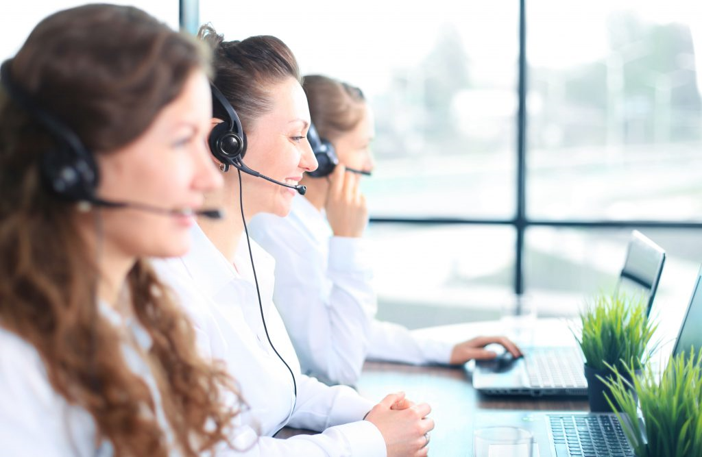 Portrait of smiling female customer service agent wearing headset with colleagues working in background at office